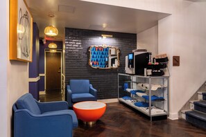 A modern hotel lobby with a black brick wall, a round orange table, blue armchairs, and a large mirror. - Hotel Ivy Boston Common (Boston)