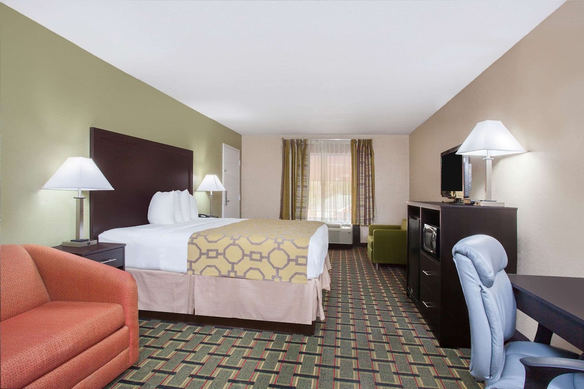 Une chambre d’hôtel comprenant un lit, deux tables de chevet avec des lampes, un bureau avec une chaise, une télévision et un sol recouvert de moquette.
