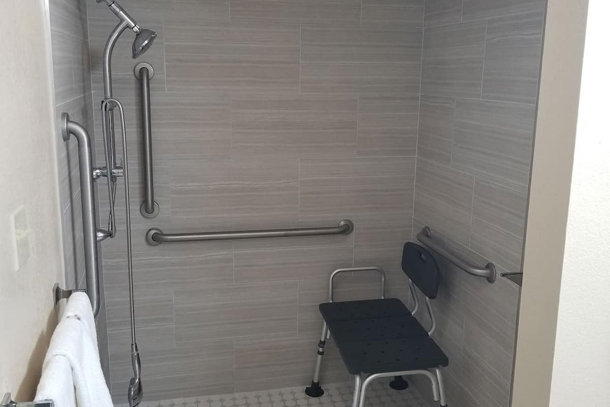 Une salle de bain équipée d’une douche, de barres d’appui, d’un banc accessible aux personnes en fauteuil roulant et d’un porte-serviettes.