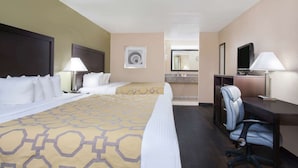 A hotel room with a large bed, two bedside tables with lamps, a desk with a chair, a television, and a bathroom visible in the background. - Baymont by Wyndham Lake City I-75 (Lake City)