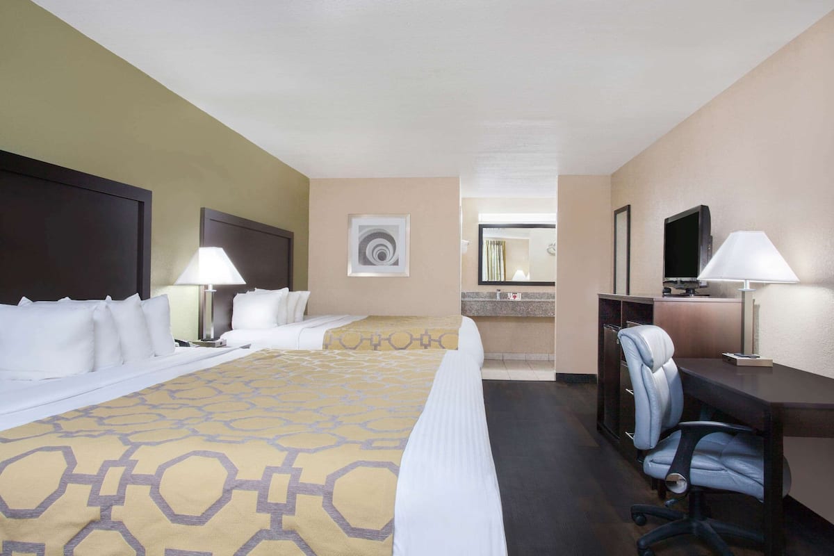 Une chambre d’hôtel avec un grand lit, deux tables de chevet avec des lampes, un bureau avec une chaise, une télévision et une salle de bain visible au fond.