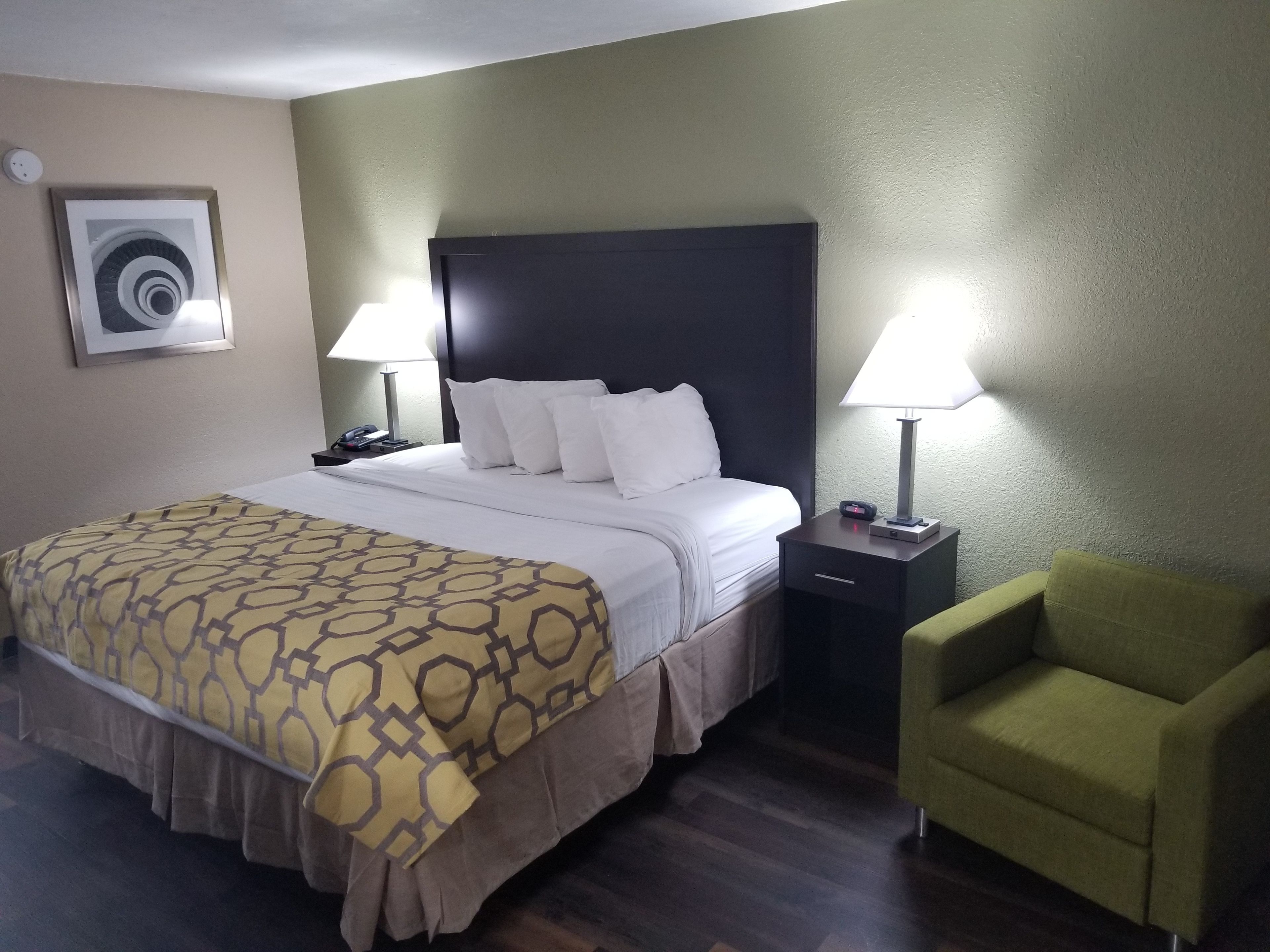 A hotel room with a large bed, two bedside tables, a green armchair, and a wall-mounted air conditioning unit.