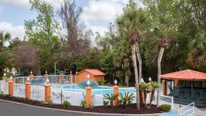 A pool area with a fenced deck, palm trees, and a small building with a red roof. - Baymont by Wyndham Lake City I-75 (Lake City)