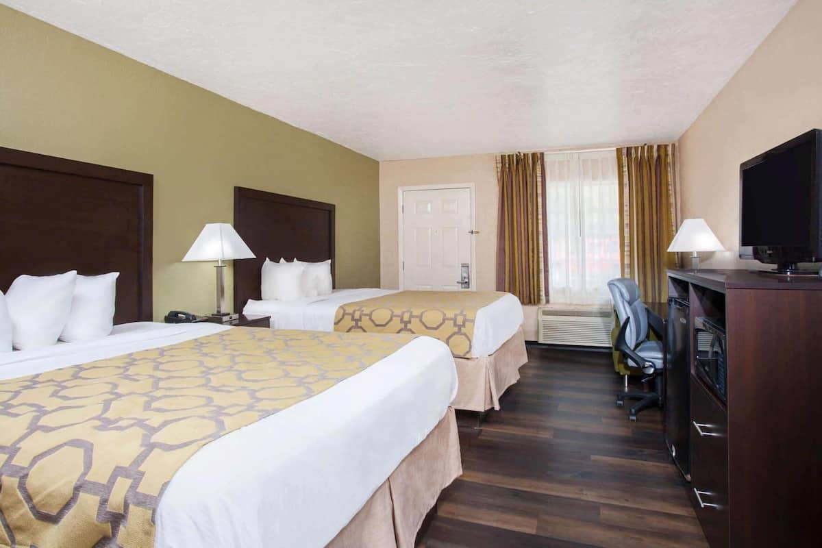 Une chambre d’hôtel avec deux lits, un bureau avec une télévision et une chaise.