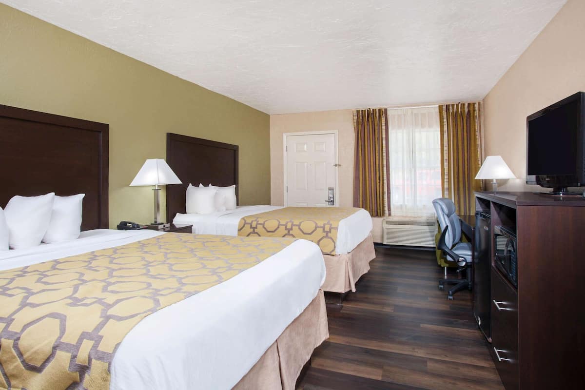 Une chambre d’hôtel avec deux lits, un bureau avec une télévision, une chaise et une lampe de bureau.