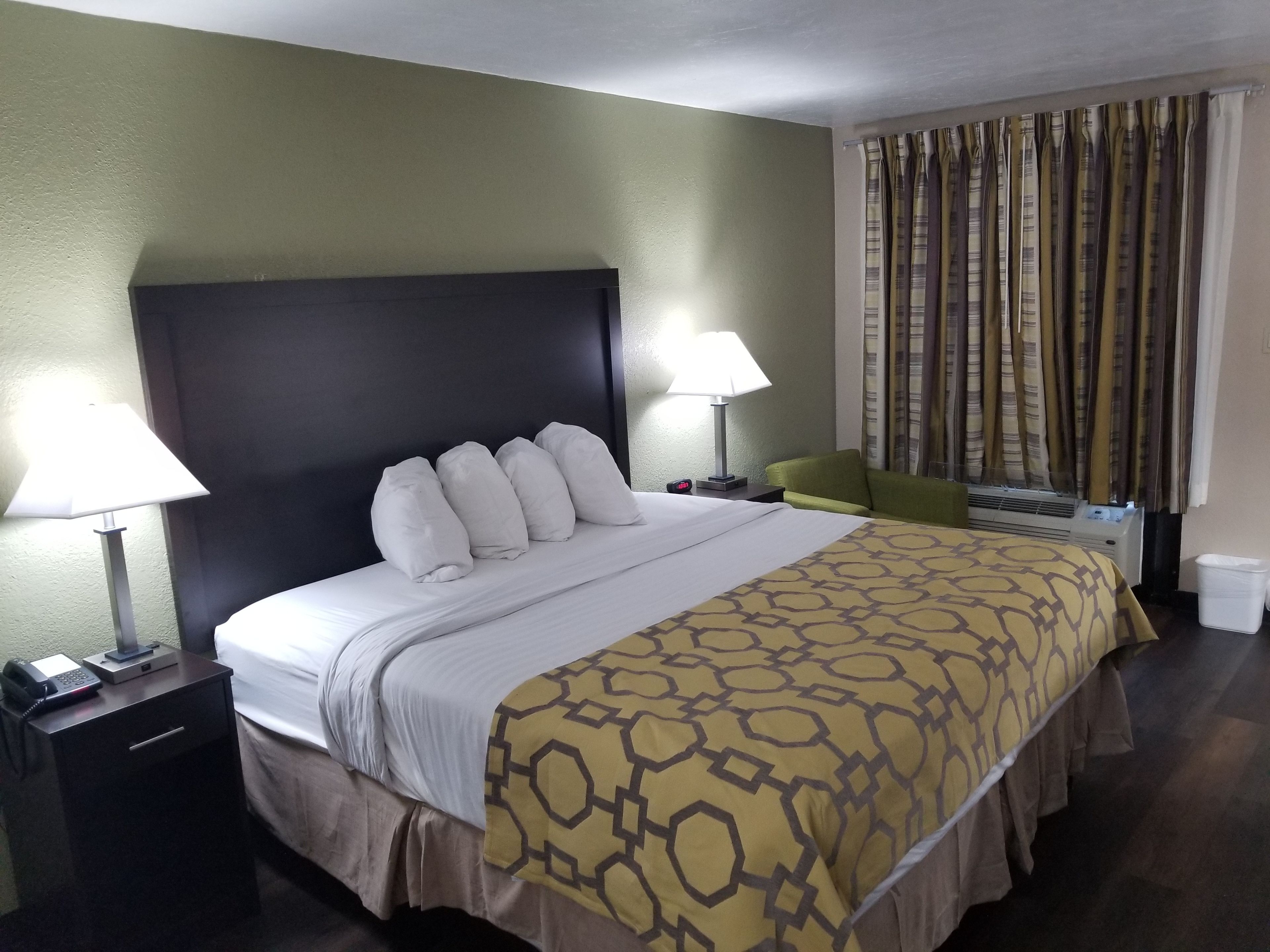 A hotel room with a large bed, two bedside lamps, a telephone, and a window with curtains.