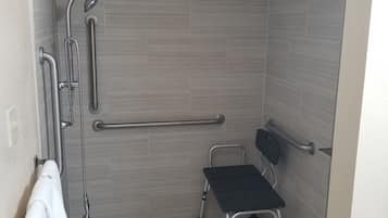 Un baño con ducha, barras de apoyo, un banco accesible para sillas de ruedas y un perchero para toallas.