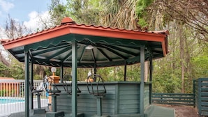 A gazebo with a red roof and green walls, surrounded by trees and a pool. - Baymont by Wyndham Lake City I-75 (Lake City)