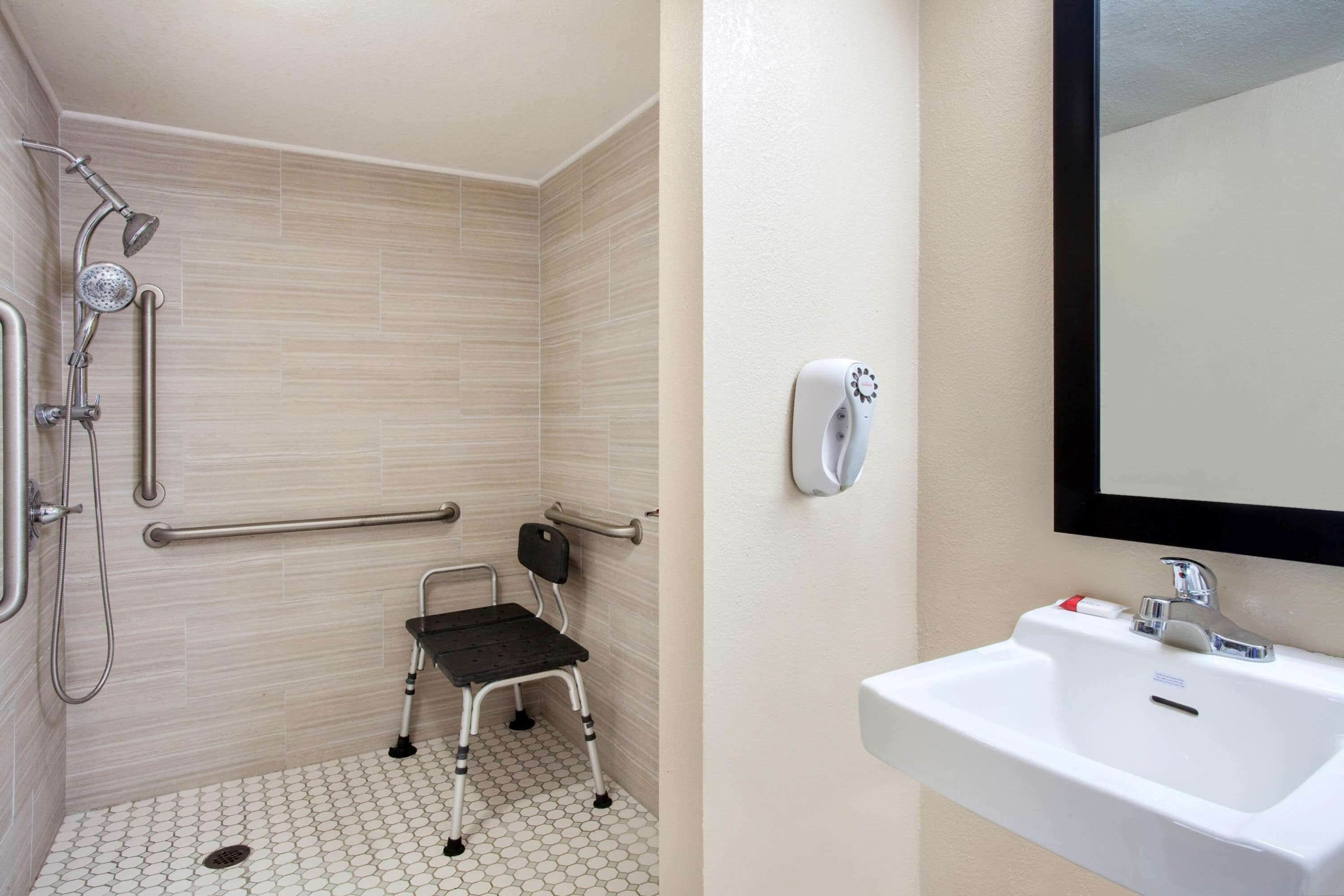 A bathroom with a white sink, a handheld showerhead, a grab bar, and a wheelchair-accessible chair.