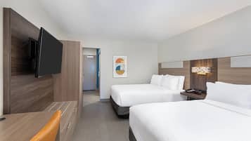 A hotel room with a bed, a desk, a television, and a door leading to another room.