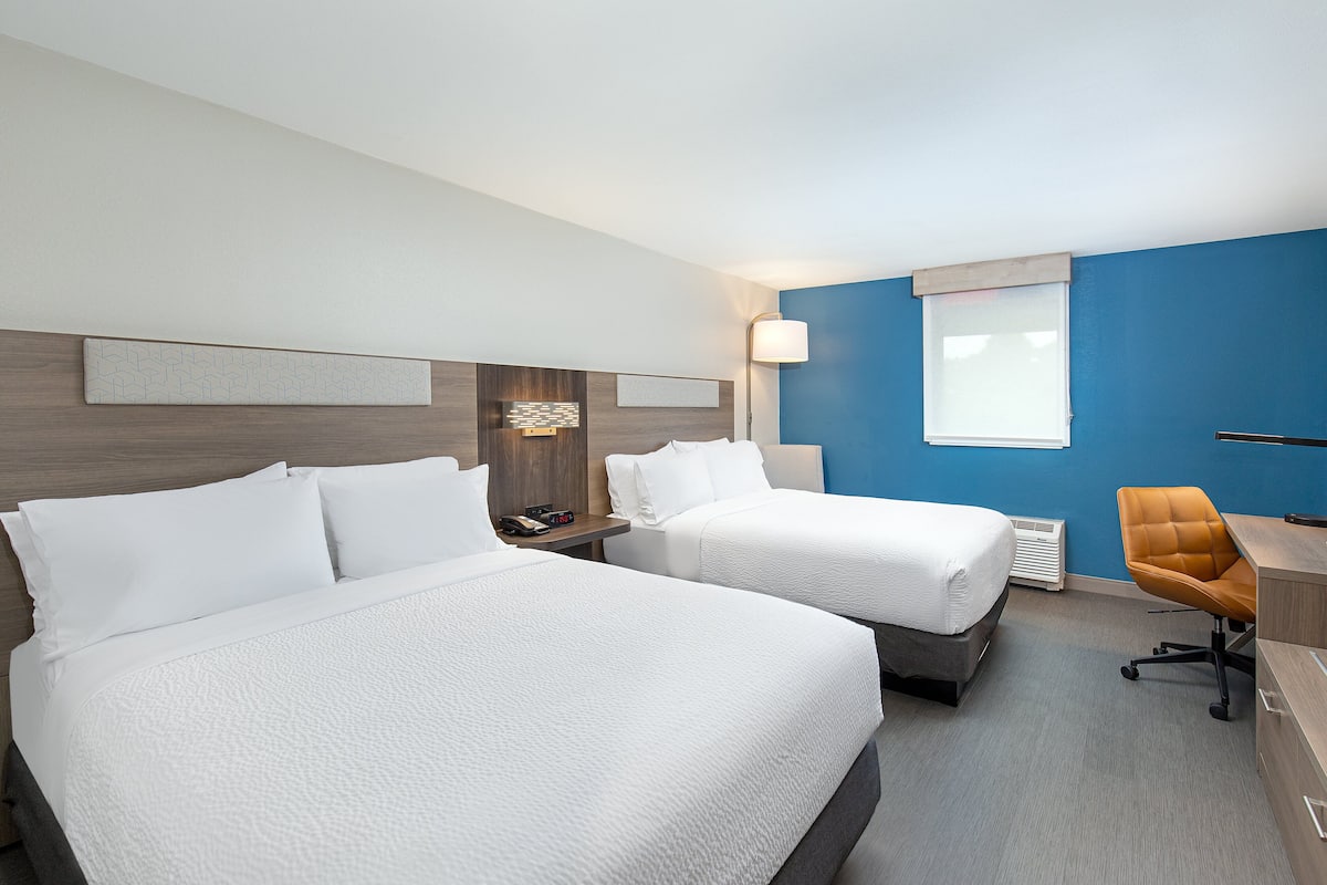A hotel room with two beds, a desk, and a chair.
