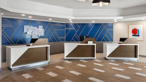 A reception area with three white reception desks, a blue geometric wall design, and modern pendant lighting.