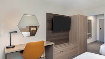 Habitación de hotel con cama, escritorio, silla, televisor, armario y espejo.