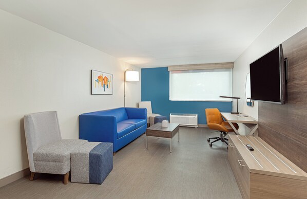 A hotel room with a blue sofa, a grey armchair, a wooden desk, and a television.