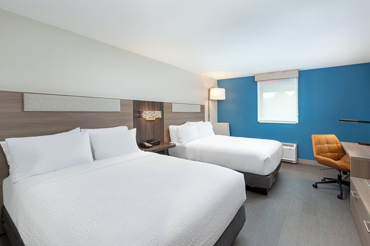 A hotel room with two beds, a desk, and a chair.