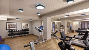 A gym with exercise equipment, a mirrored wall, and a wooden floor.