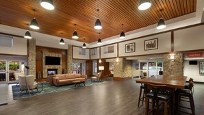 A spacious lobby with a wooden ceiling, stone walls, a fireplace, a television, and a dining area.