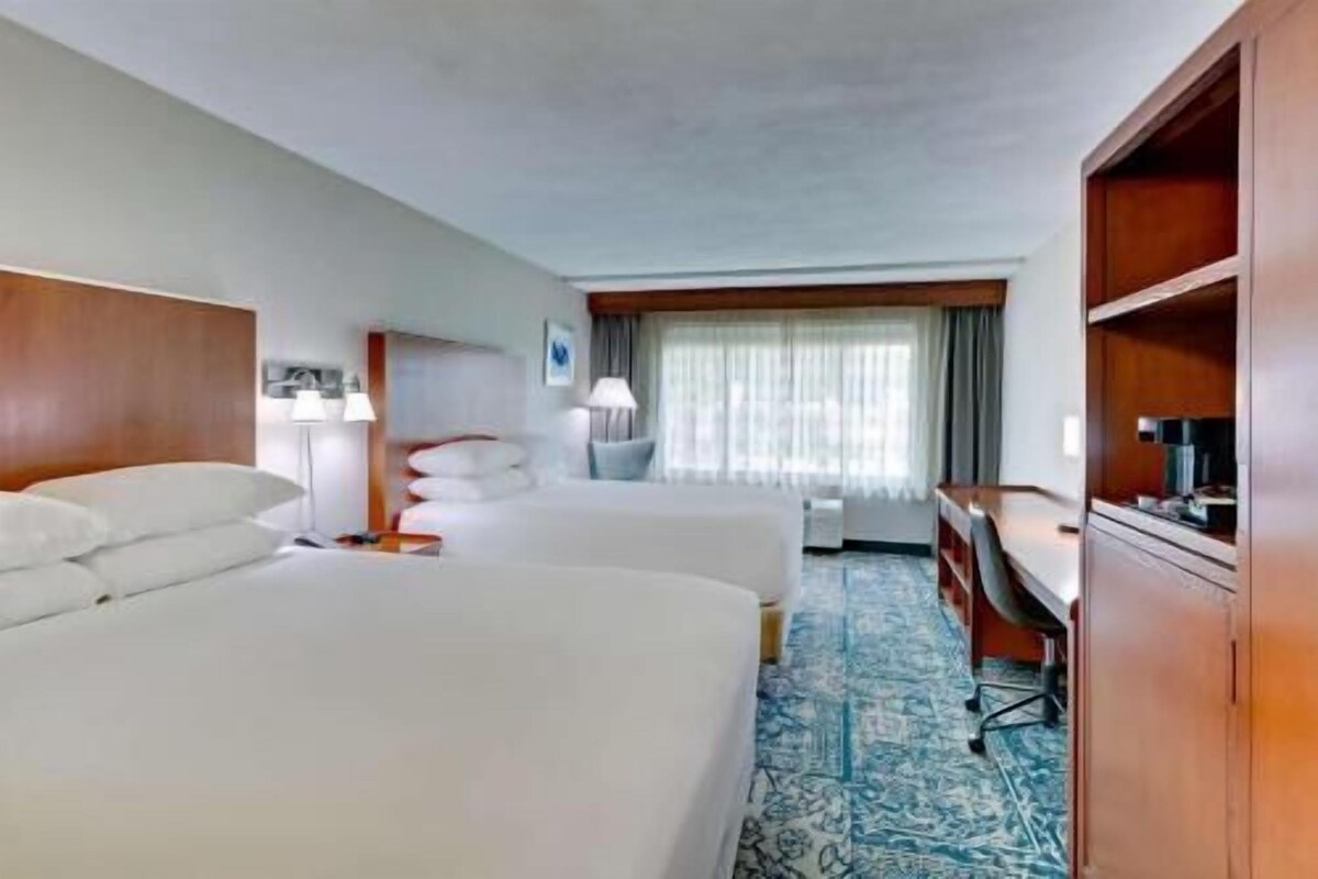 A hotel room with two beds, a desk, a chair, a lamp, and a television.