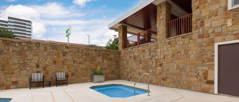 Una piscina con un muro de piedra, dos sillas y una pequeña mesa.