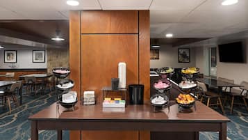A buffet setup with various food items, a stack of white plates, and a trash bin.