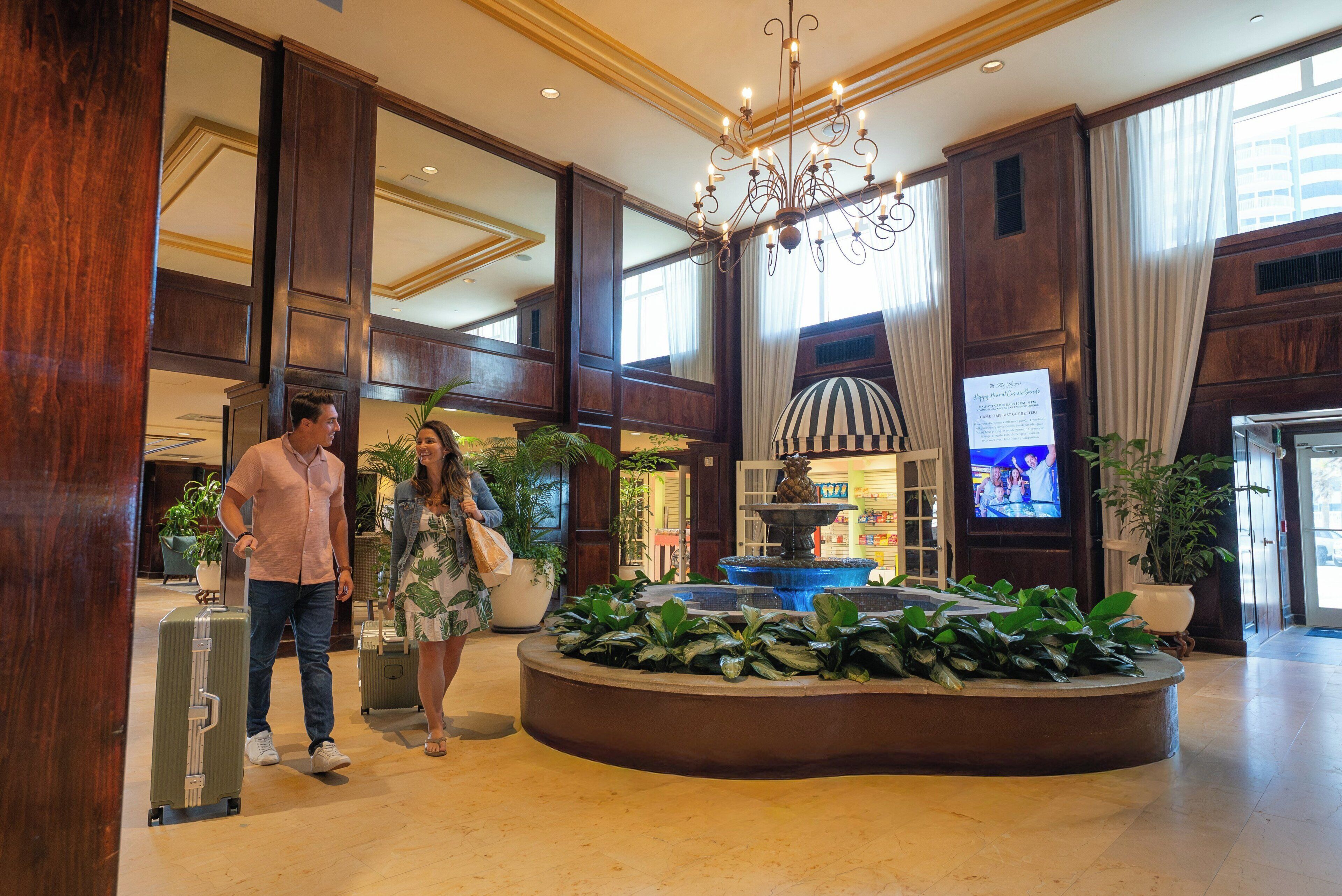 A spacious lobby with a grand chandelier, a fountain, and a television screen.