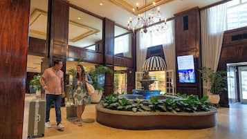 A spacious lobby with a grand chandelier, a fountain, and a television screen.
