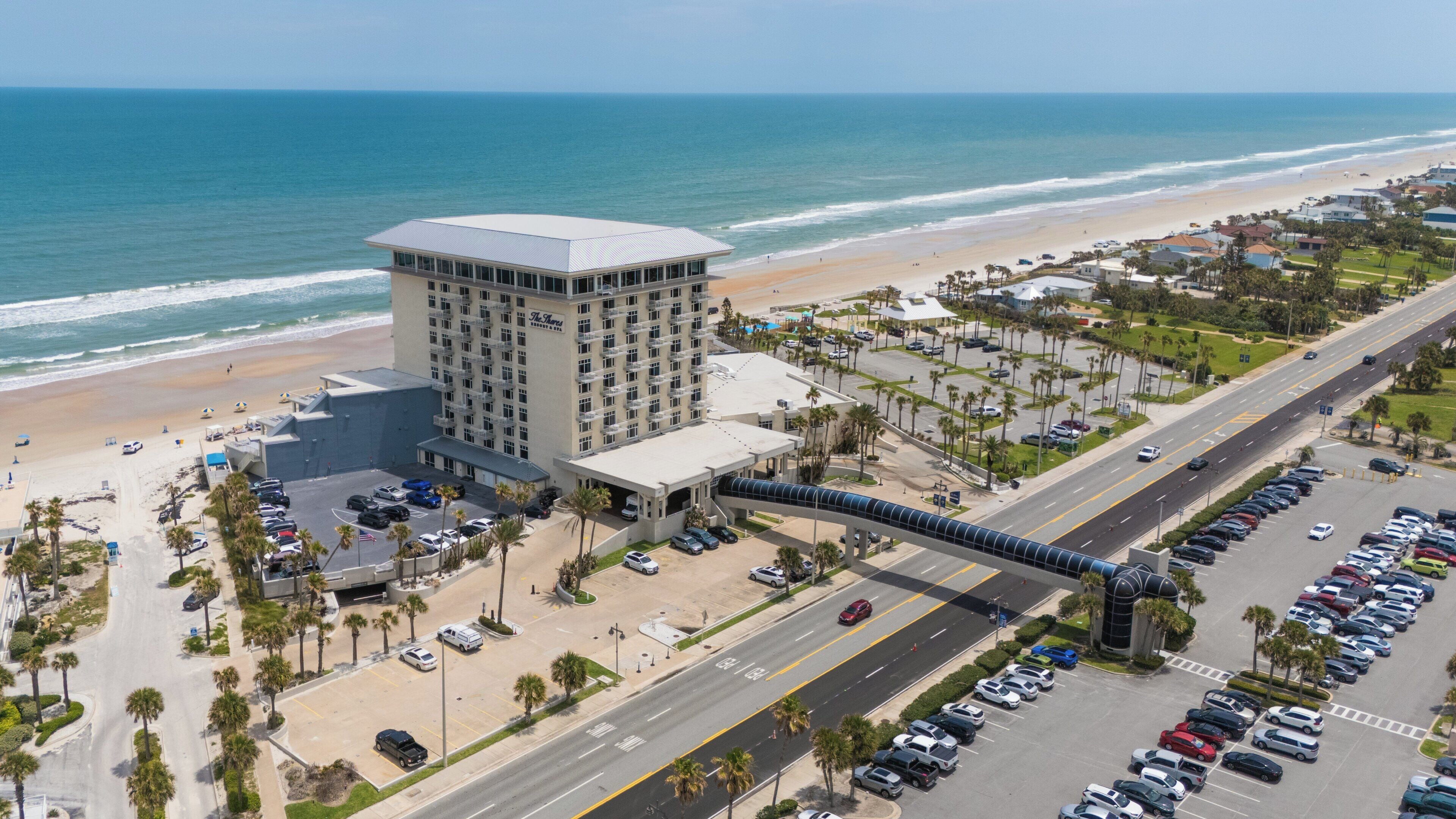Un hotel junto a la costa con estacionamiento, una carretera y una playa.