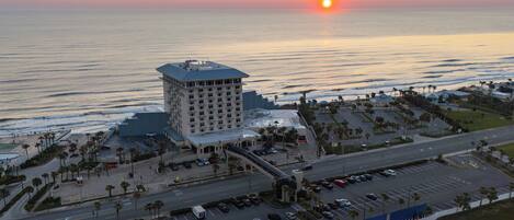 Un hotel de gran altura con estacionamiento y vista al océano al atardecer.