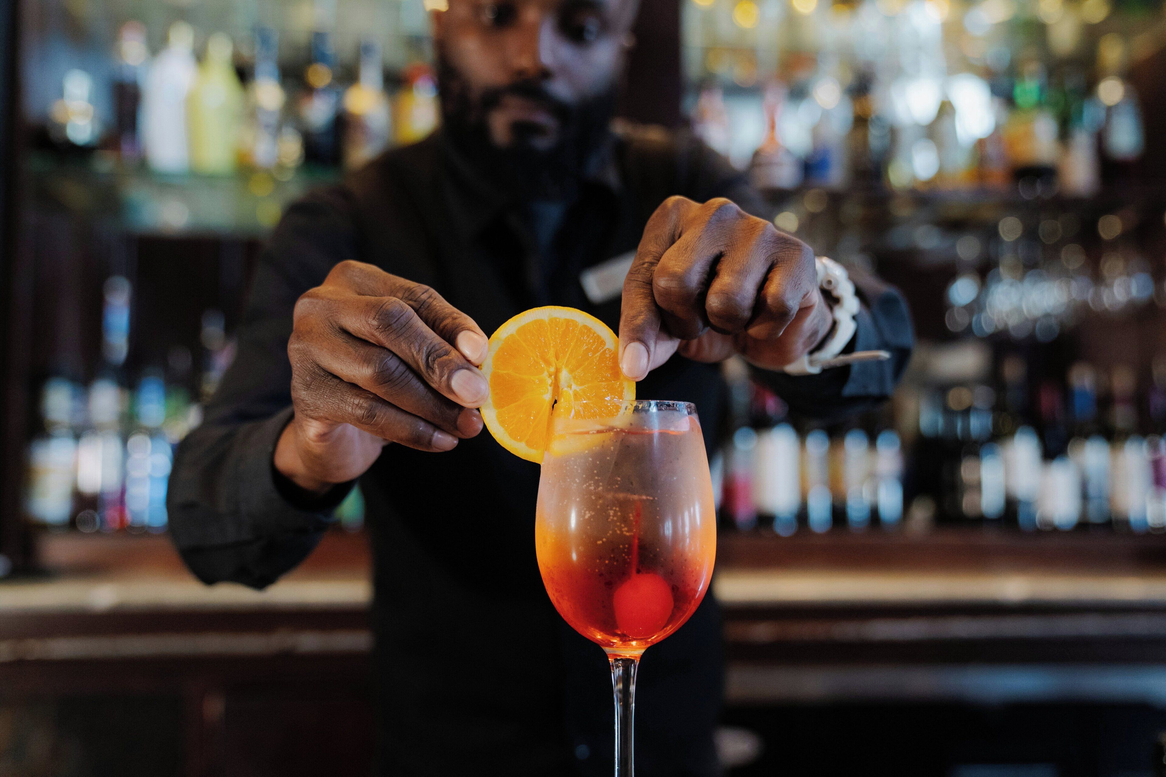 A bartender preparing a cocktail with an orange slice garnish.