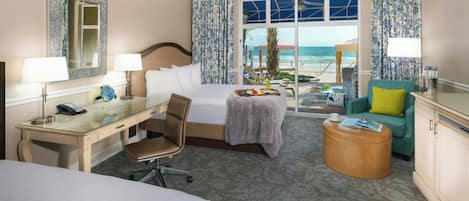 A hotel room with a bed, desk, chair, and a view of the beach.