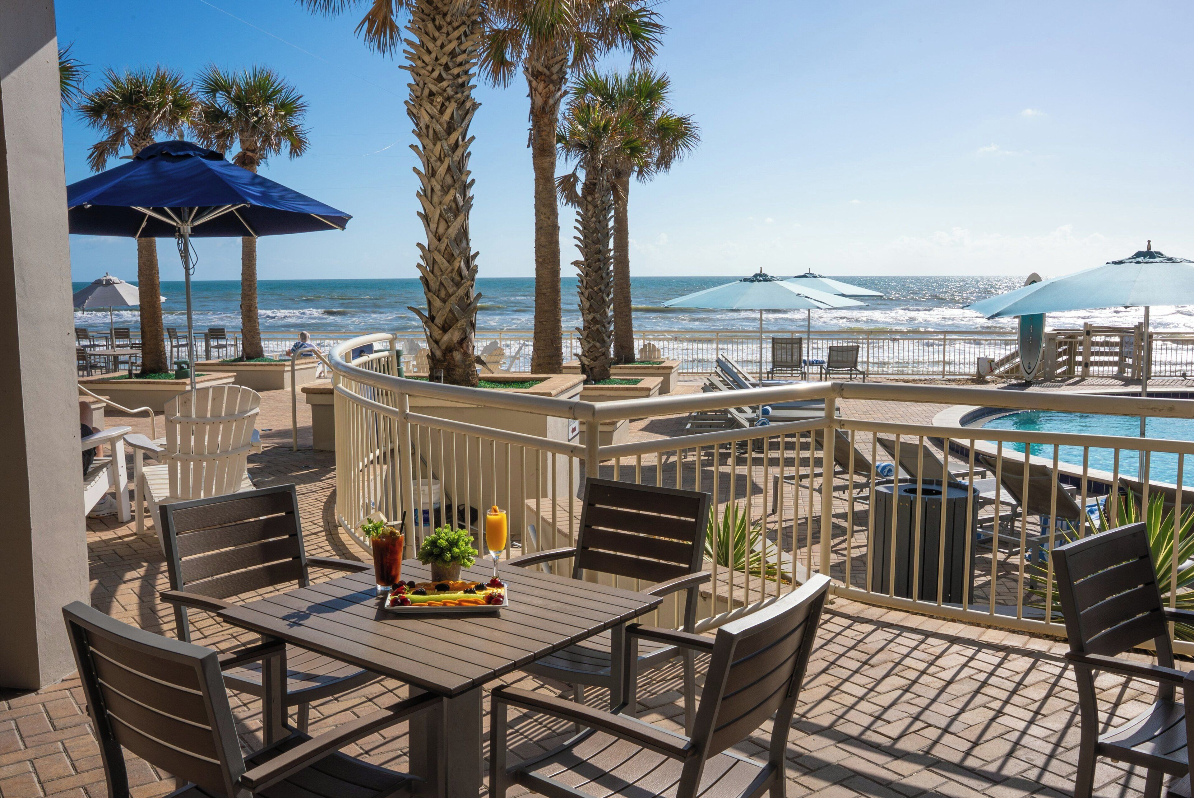 A patio with a table set for two, overlooking a pool and the ocean.