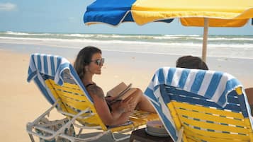 Two beach chairs with striped towels, a beach umbrella, and a view of the ocean.