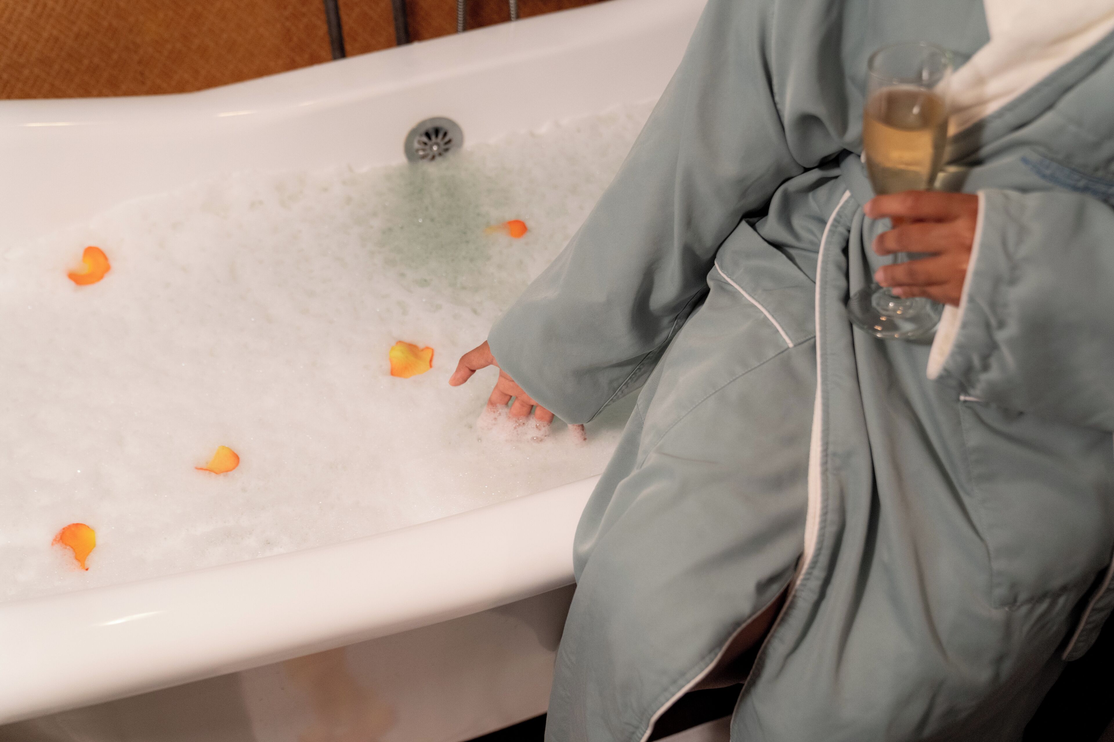 Une personne vêtue d’une robe, assise dans une baignoire remplie de pétales de rose et de mousse.