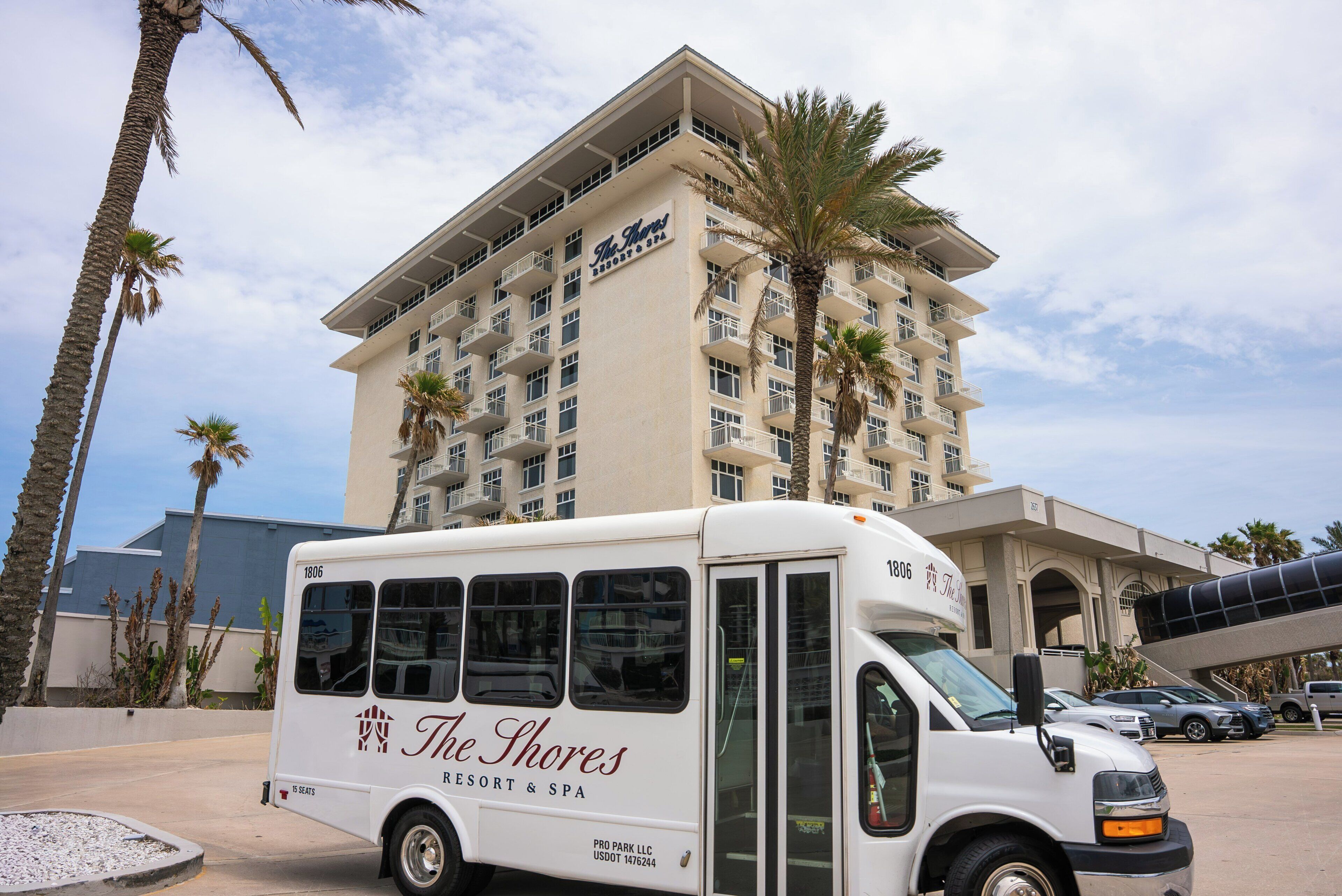 A white bus with 'The Shores Resort & Spa' branding parked in front of a multi-story hotel building.