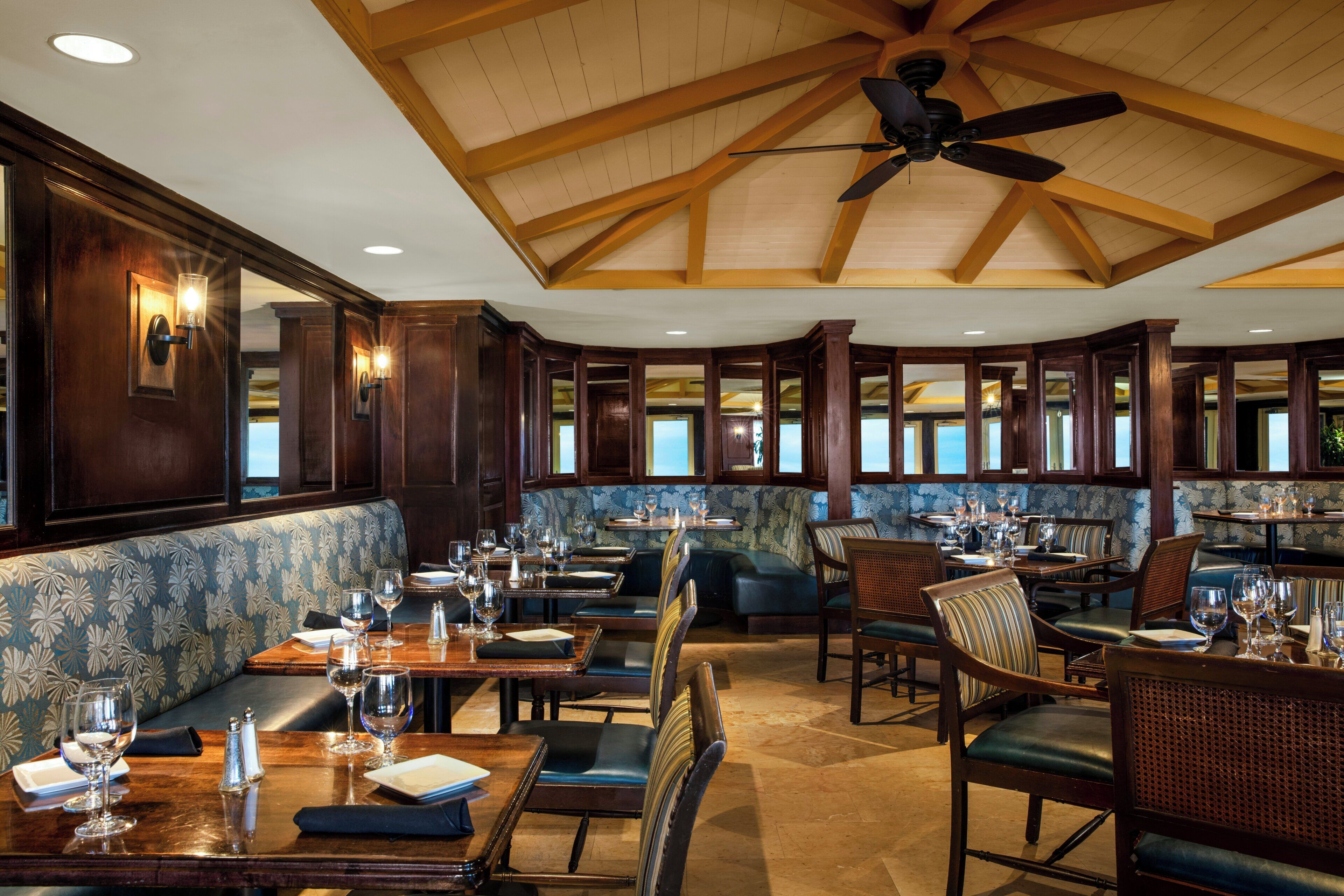 A restaurant with wooden ceiling beams, patterned wallpaper, and a variety of seating options including booths and tables.
