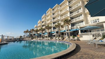 A hotel with a swimming pool, multiple balconies, and lounge chairs.
