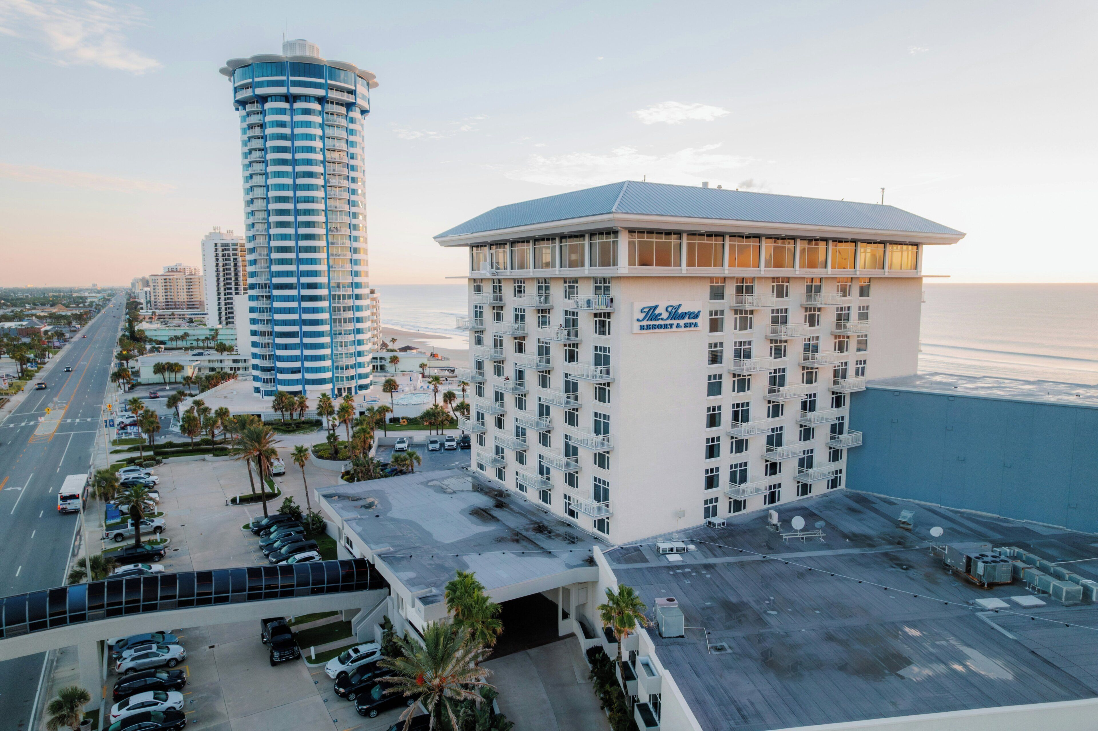 A hotel with a large parking lot, a beachfront view, and a prominent tower building in the background.