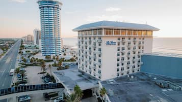 A hotel with a large parking lot, a beachfront view, and a prominent tower building in the background.