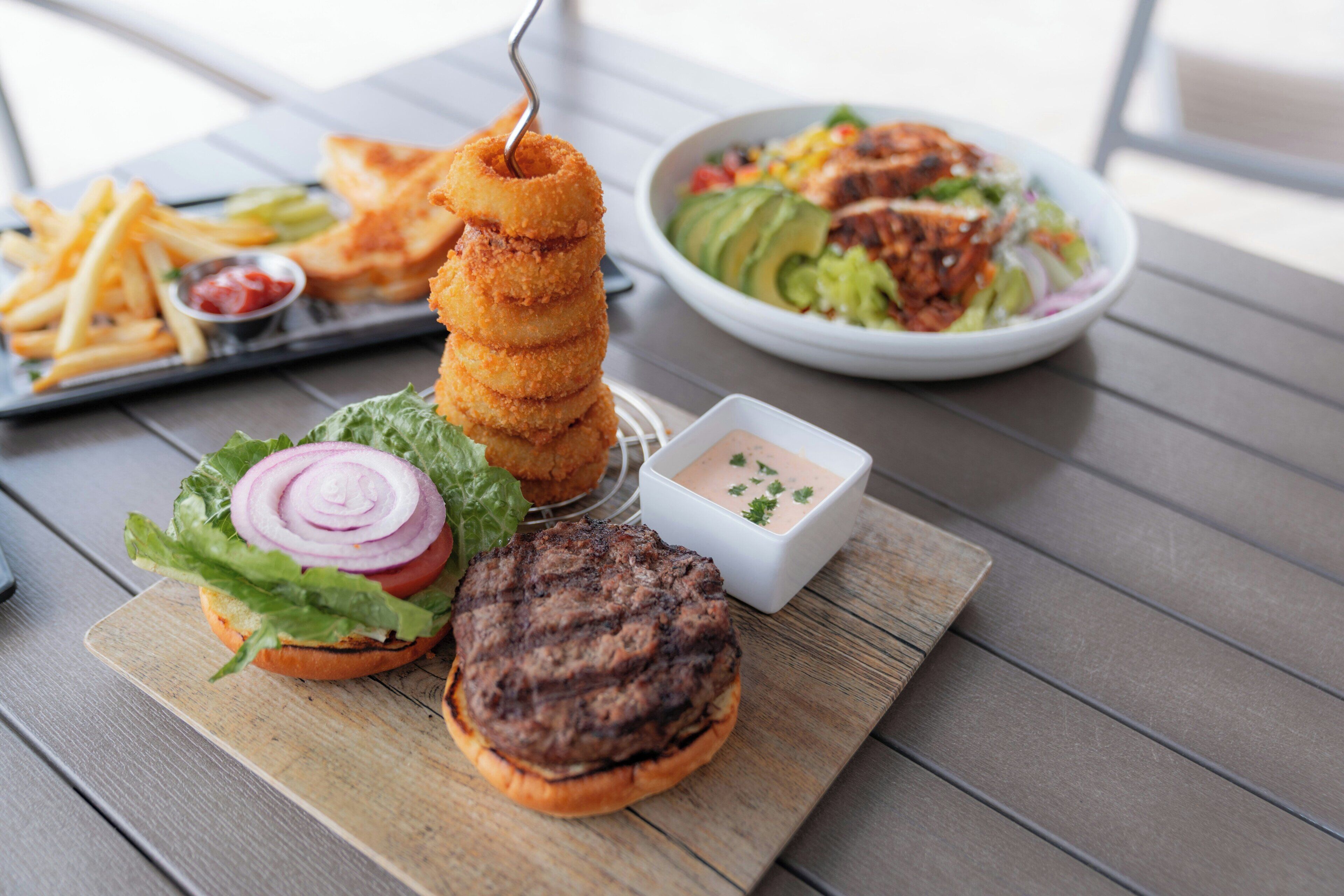 A meal consisting of a burger, onion rings, fries, and a salad on a wooden table.