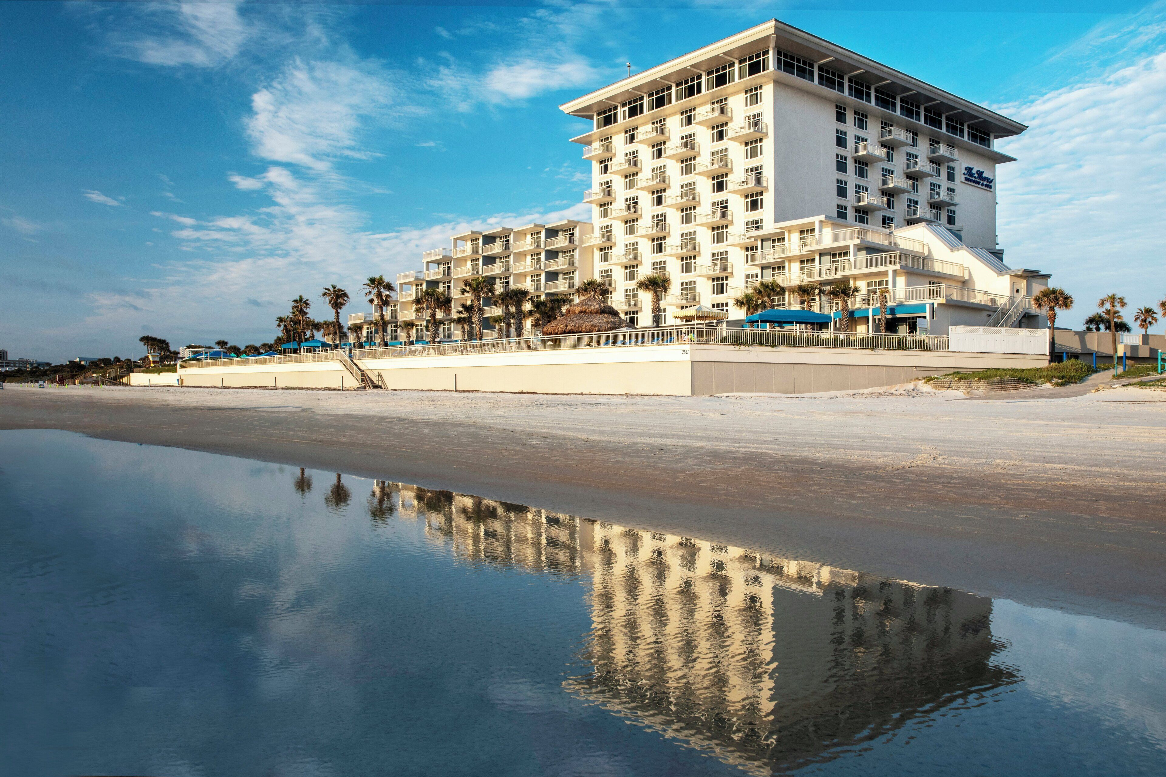 A beachfront hotel with multiple balconies and a reflection in the water.