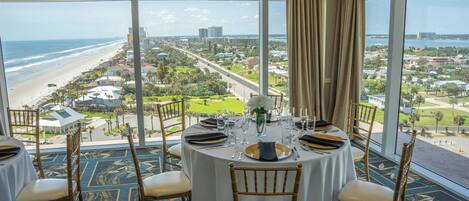 Mesa de comedor lista para cuatro personas con vista a la playa y al paisaje urbano.