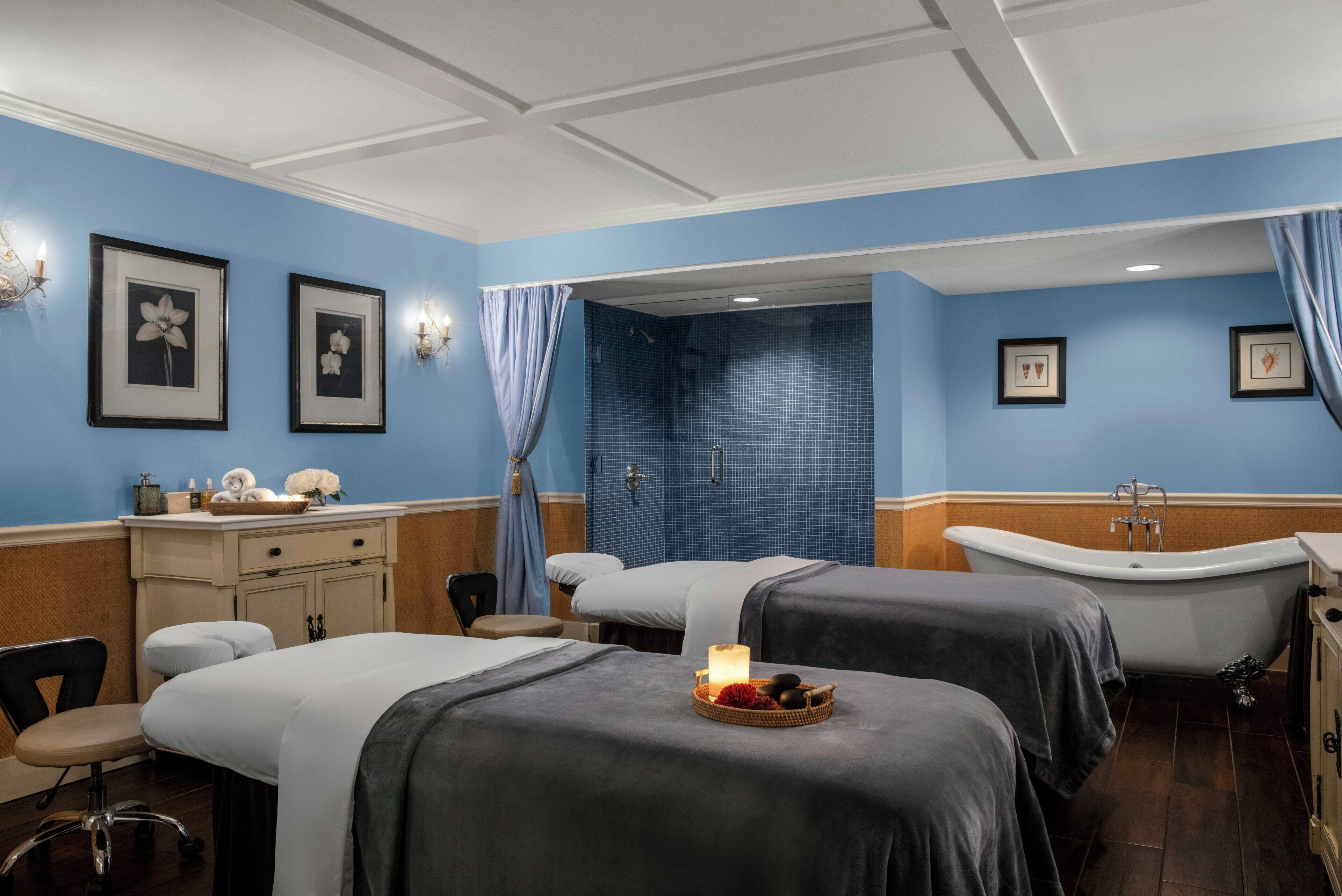 Habitación de hotel con dos camas, una bañera, un escritorio con silla y una pared decorada con cuadros.