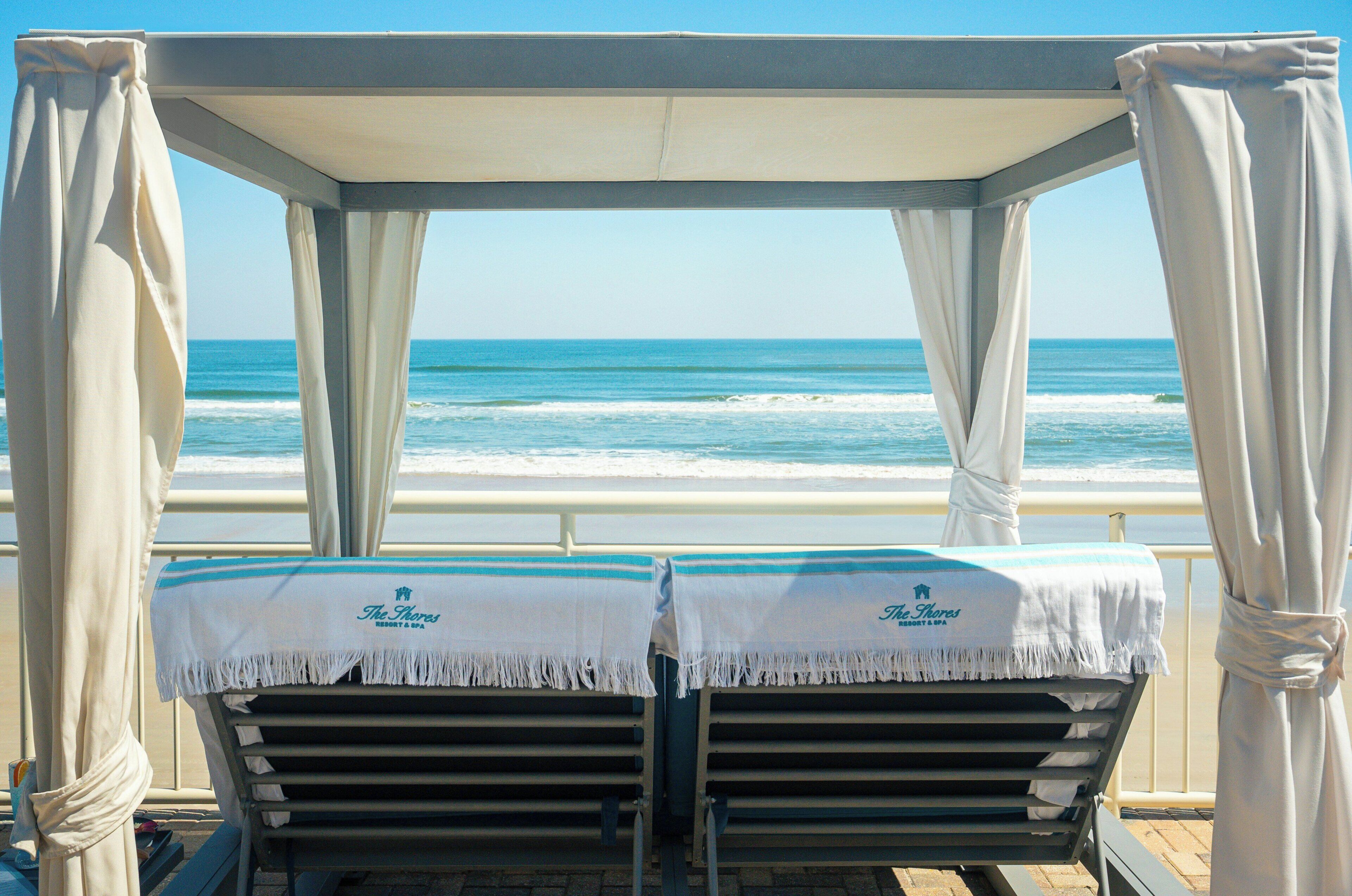 Dos tumbonas con vista al océano, una sombrilla y un cartel que dice 'The Shores Resort & Spa'.