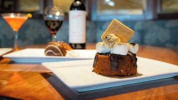 A dessert with marshmallows and chocolate on a plate, a bottle of wine, and a martini glass on a table.