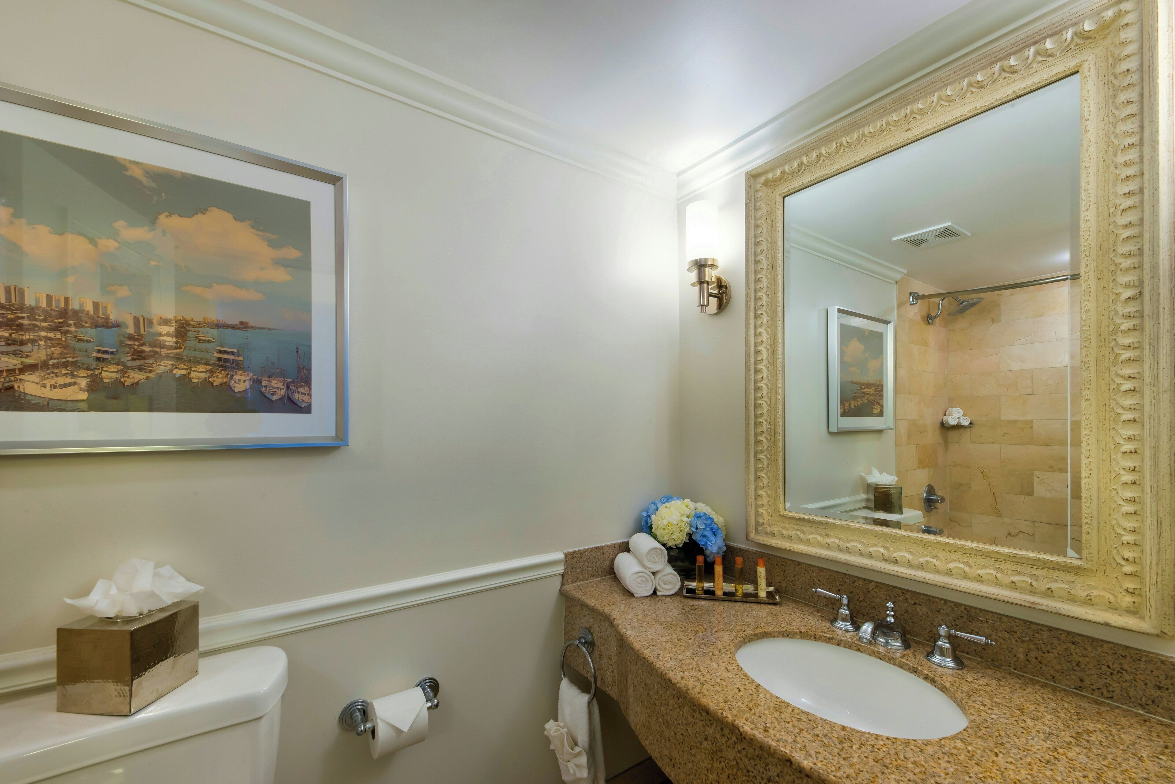 Une salle de bain avec un grand miroir, un lavabo, des toilettes et un tableau encadré au mur.