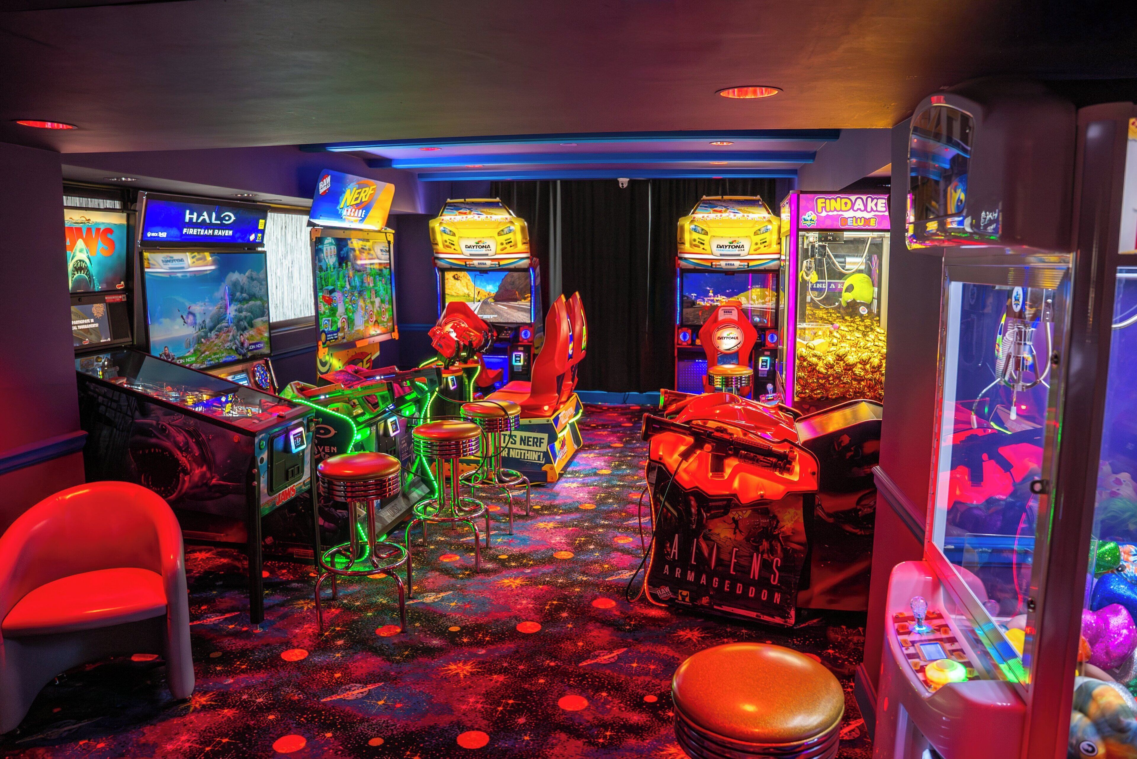 A gaming arcade with various machines, including racing and claw-pit games, and a neon-lit floor.