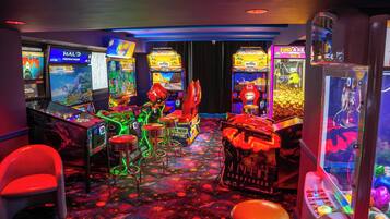 A gaming arcade with various machines, including racing and claw-pit games, and a neon-lit floor.