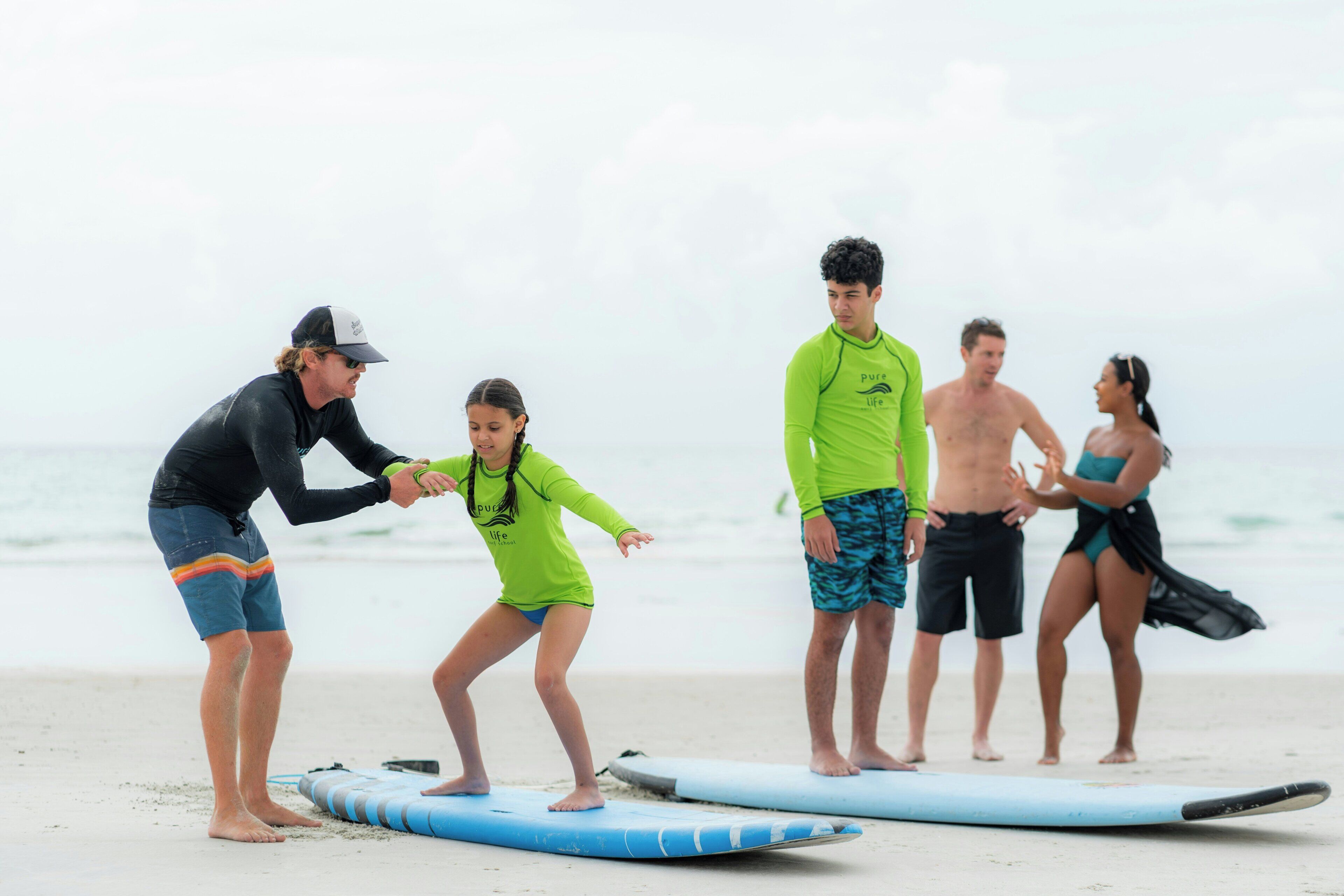 Un groupe de personnes se trouve sur une plage, certaines debout et d’autres assises, et elles ont toutes des planches de surf.
