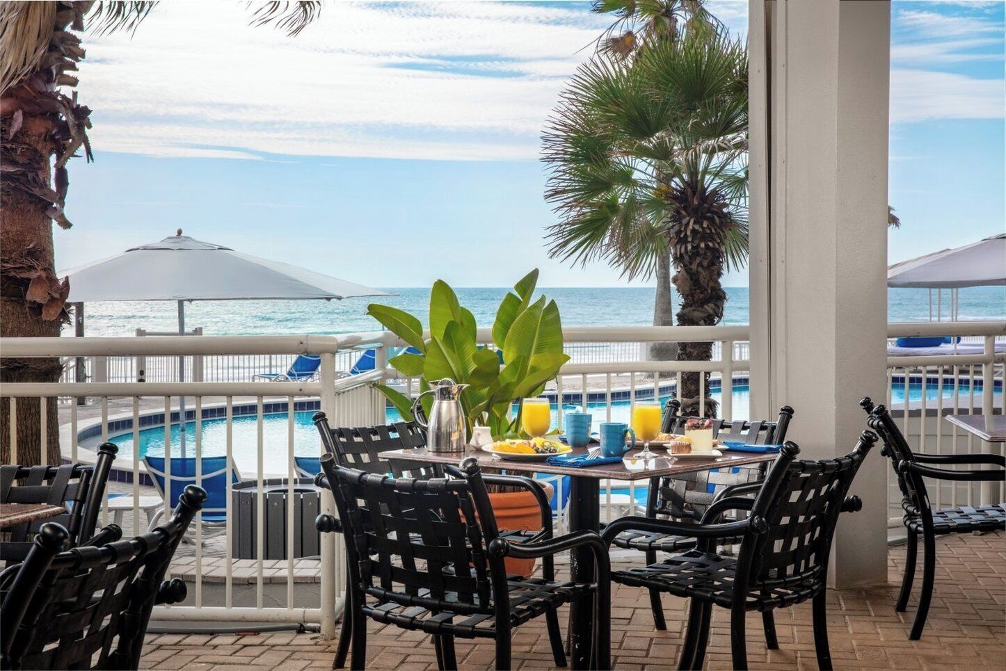 Zona junto a la piscina con mesa dispuesta para el desayuno, con vistas a la piscina y al océano.