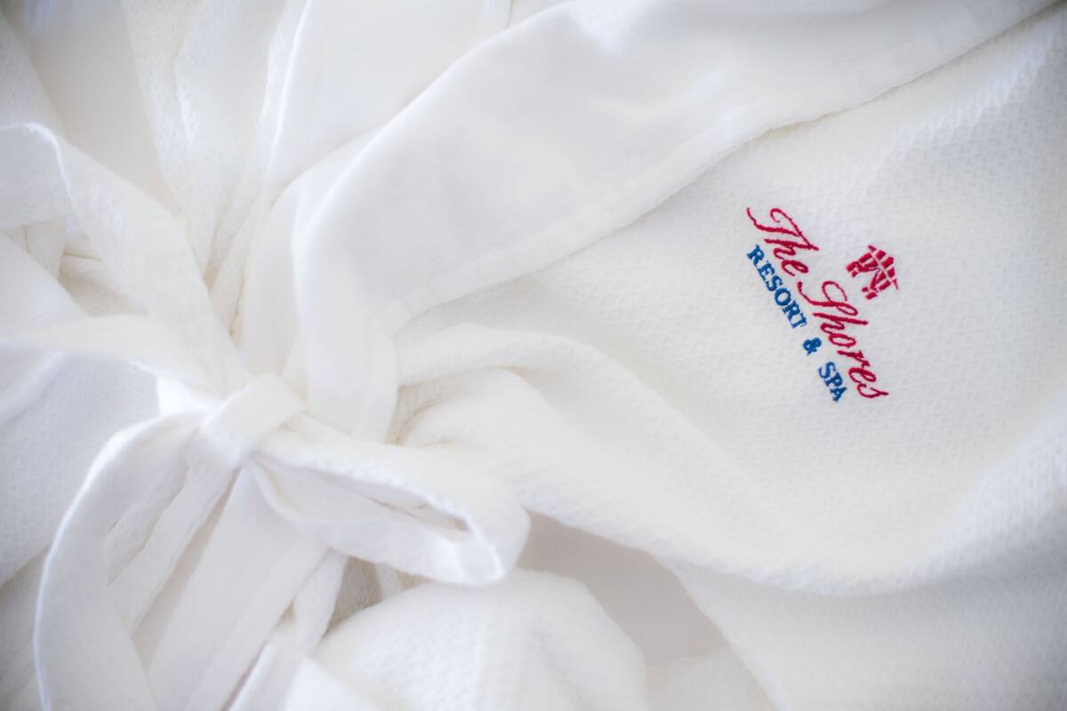 A white towel with embroidered text reading "The Shore Resort Spa".